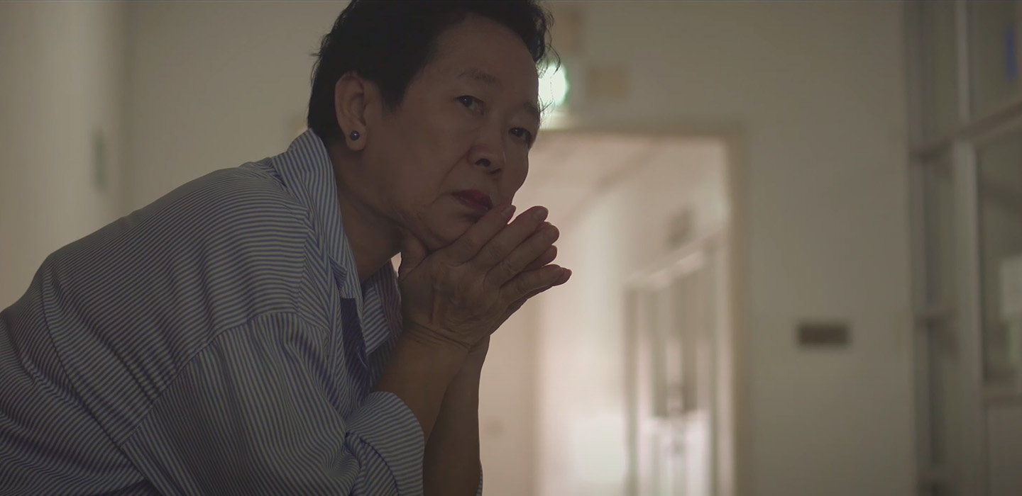Video screengrab of person sitting in hallway with chin on hands, looking concerned.