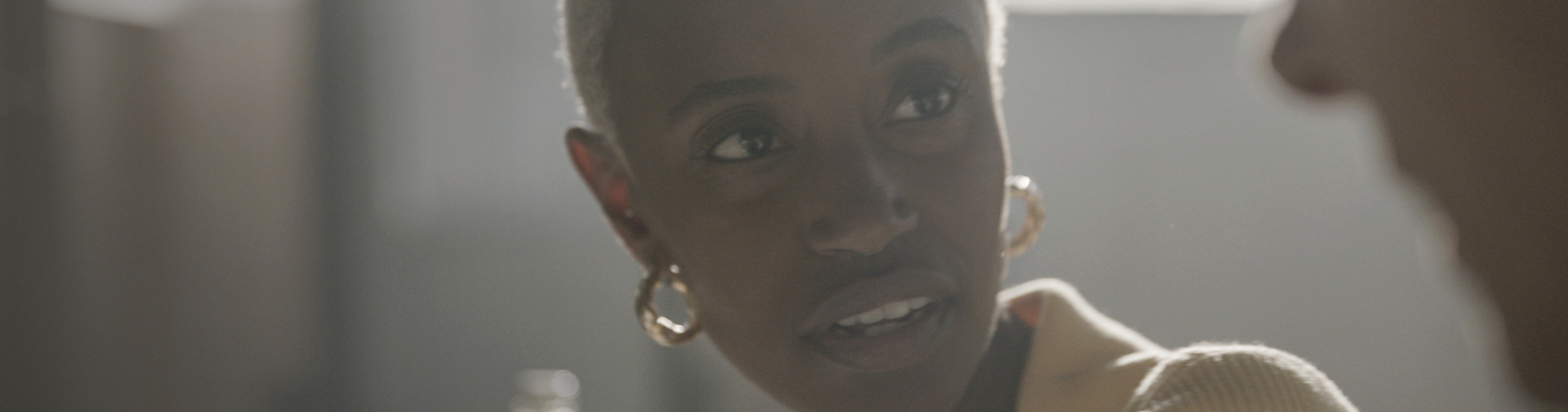 Woman in sunlight, with hoop earrings, looking at a conversation partner.