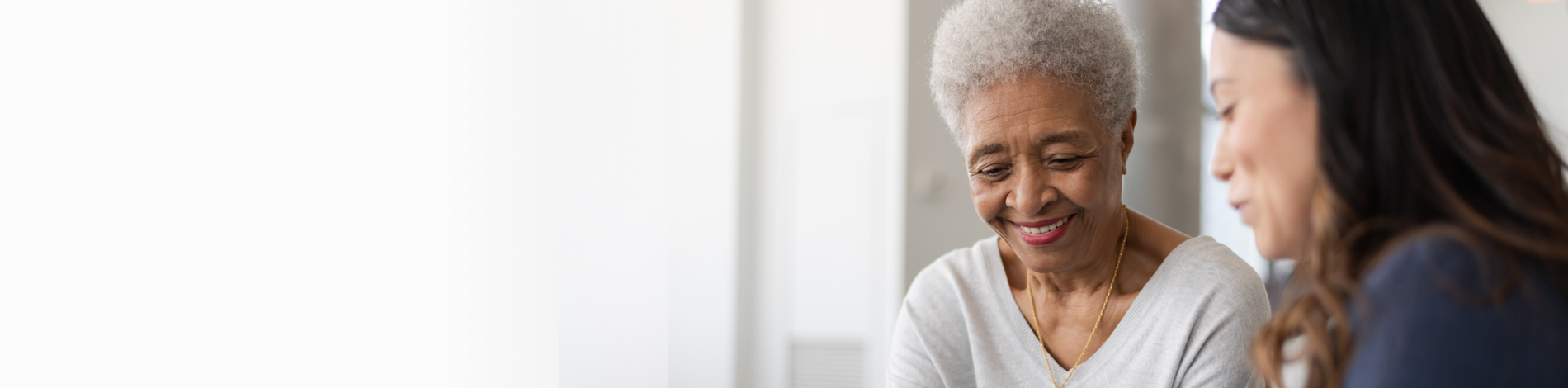 Older woman smiling and looking down, in conversation with female healthcare worker.