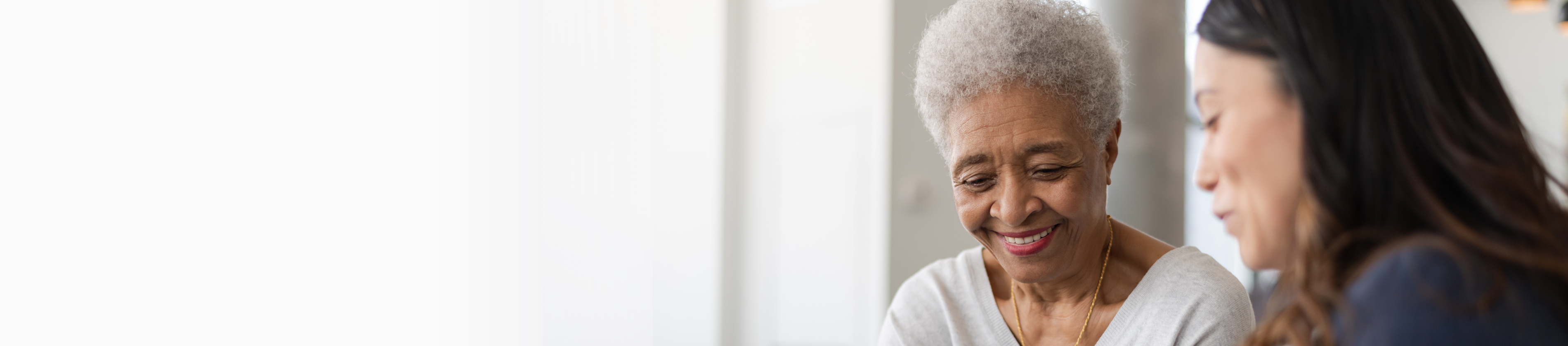 Older woman smiling and looking down, in conversation with female healthcare worker.