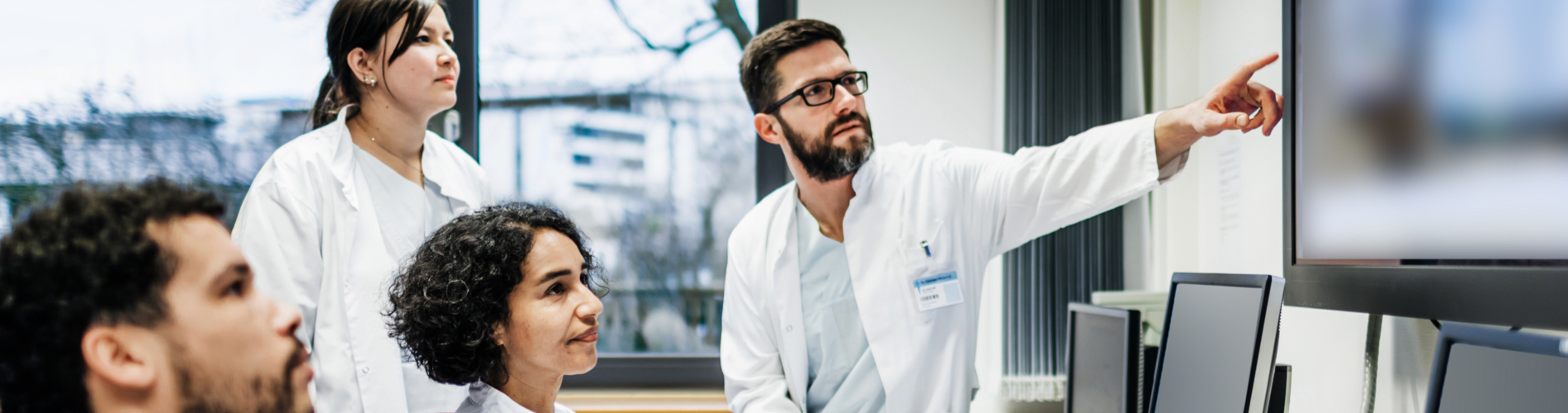 Four healthcare professionals, with one pointing and the others looking in that direction.